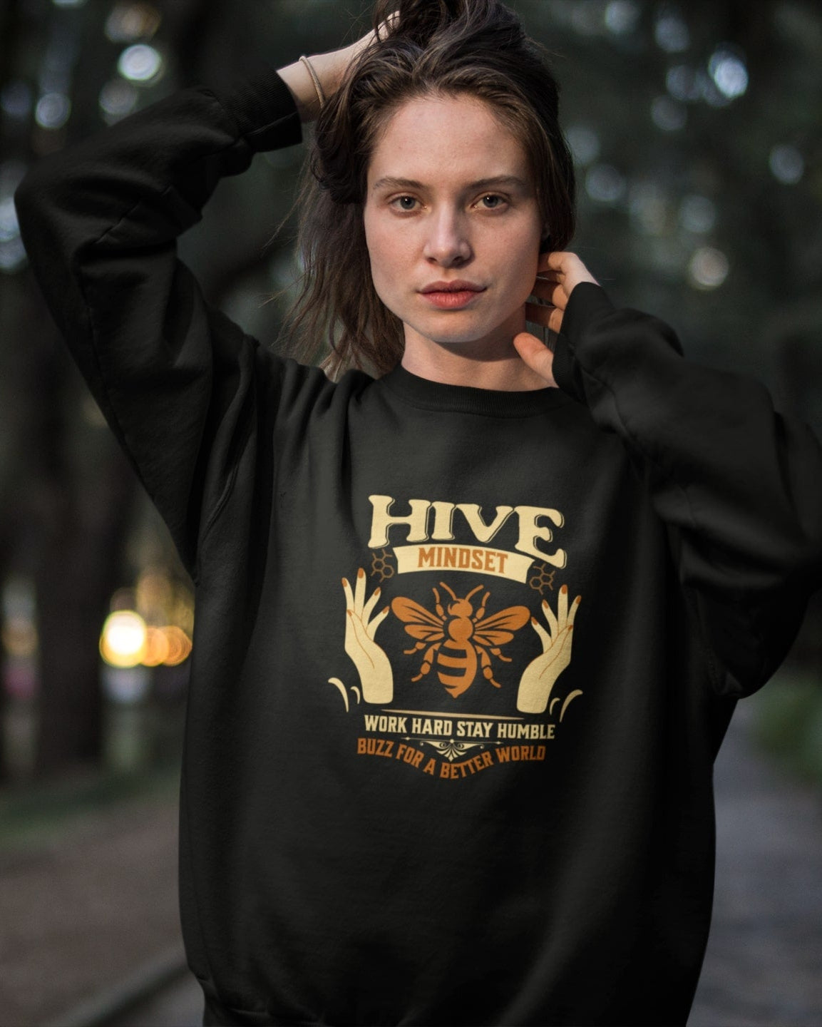 Person wearing a black hoodie with 'Hive Mindset' graphic design outdoors.