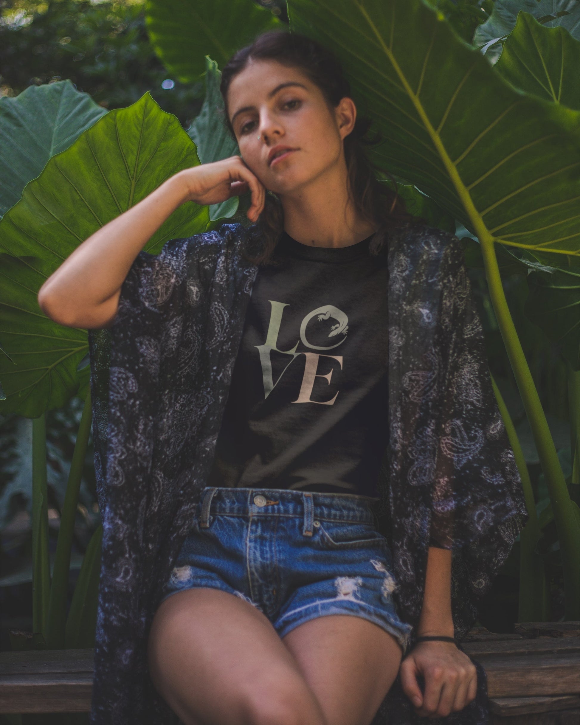 Woman sitting among large green leaves wearing a black t-shirt with 'LOVE' printed on it.